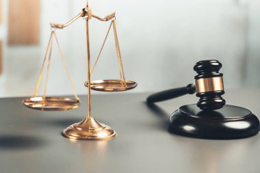 Adalet ve hukuki otorite kavramının simgesi olarak mahkeme kütüphanesinde parlak altın dengeli ölçek ve ahşap tokmak avukat ve yargıç tarafından eşitlik ve adil yargılamayı yansıtıyor. denge