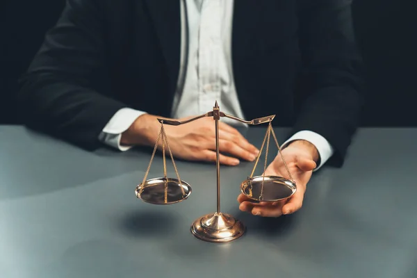 stock image Lawyer in a black suit sits attentively on his office desk with a golden scale balance, symbol of legal justice and integrity, balanced and ethical decision making in the court of law. equility