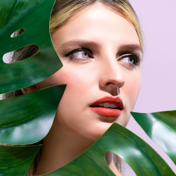 stock image Closeup woman with perfect clean skin and alluring flawless natural soft facial makeup holding green leave monstera. Natural skincare treatment beauty or spa concept in pink isolated background.