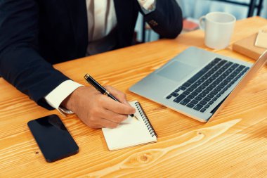 Modern ofis masasındaki modern profesyonel iş adamı çalışmak ve notlar yazmak için dizüstü bilgisayar kullanıyor. Ofisinde bilgisayar defteri üzerinde çalışan çalışkan bir ofis çalışanı. coşkulu