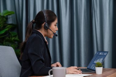 Bilgisayarında mikrofon ve kulaklıkla Asyalı çağrı merkezi çalışıyor. Kadın operatör istisnai müşteri hizmetleri sunar. Destek veren çağrı merkezi ajanı, müşteriye soruşturmada yardım ediyor. Coşkulu.