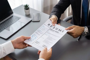 Resmi ofiste takım elbise giyen kendine güvenen bir adam, iş görüşmesi sırasında özgeçmiş kağıtlarını tutuyor. Sorular soran, aday yeterliliği ve iş için uygunluk değerlendirmesi yapan bir muhabir. Coşkulu