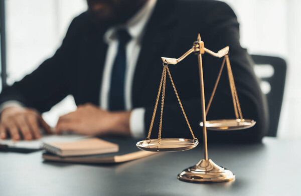 Focus shiny golden balanced scale on blurred background of lawyer working in his desk at law firm office. Scale balance for righteous and equality judgment by lawmaker and attorney. Equilibrium