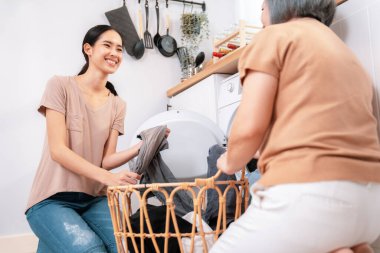 Daughter and mother working together to complete their household chores near the washing machine in a happy and contented manner. Mother and daughter doing the usual tasks in the house.