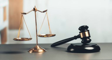 Adalet ve hukuki otorite kavramının simgesi olarak mahkeme kütüphanesinde parlak altın dengeli ölçek ve ahşap tokmak avukat ve yargıç tarafından eşitlik ve adil yargılamayı yansıtıyor. denge