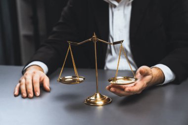Lawyer in a black suit sits attentively on his office desk with a golden scale balance, symbol of legal justice and integrity, balanced and ethical decision making in the court of law. equility clipart