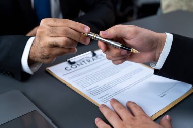 İş anlaşması yapılırken iki işadamı masanın karşısında oturuyor. Şirket avukatı, sözleşmeyi imzalaması için müvekkiline ya da ortağına kalem veriyor ve anlaşmayı imzayla imzalıyor. Coşkulu