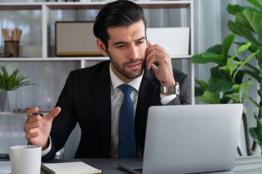 Çalışkan işadamı, ofisindeki dizüstü bilgisayarla cep telefonlu, modern, çalışkan ofis çalışanı yaşam biçimi konsepti olarak çalışırken müşterileriyle telefonda konuşmakla meşgul. Coşkulu