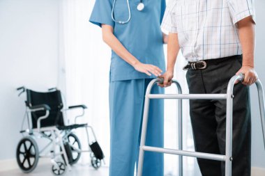 Physiotherapist assists her contented senior patient on folding walker. Recuperation for elderly, seniors care, nursing home.