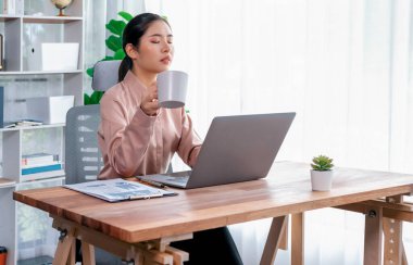 Modern ofis masasındaki Asyalı hevesli genç iş kadını çalışmak ve notlar yazmak için dizüstü bilgisayar kullanıyor. Çalışkan ve çekici ofis hanımı ofisinde bilgisayar defteri üzerinde çalışıyor..