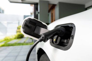 Closeup electric vehicle plugged-in with cable from charging point powered for progressive concept by alternative clean energy rechargeable EV car at home charging station.