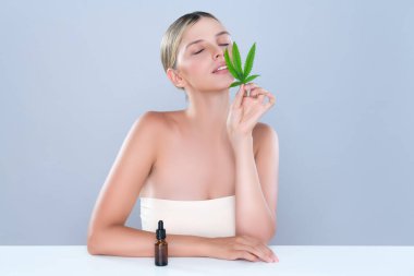 Alluring portrait of beautiful woman in isolated holding green leaf with marijuan extracted bottle for skincare treatment product. Cannabis CBD oil for cosmetology and beauty concept.