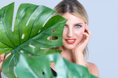 Closeup woman with perfect clean skin and alluring flawless natural soft facial makeup holding green leave monstera. Natural skincare treatment beauty or spa concept in isolated background.