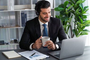Erkek çağrı merkezi operatörü ya da telesales temsilcisi ofis masasında otururken kulaklık takıyor ve müşteri desteği sağlayan ya da ikna edici satış yapan müşteriyle sohbet ediyor. coşkulu