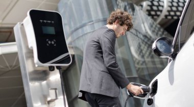 Below view closeup image of progressive black suit businessman recharge battery of his electric vehicle from public charging station. Renewable and alternative energy powered car concept.