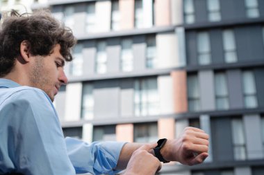 İlerici genç işadamı, dokunmatik ekranı kullanarak zamanı kontrol ediyor, şehirdeki interneti tarıyor. Mobil uygulamalı elektrikli el aleti kavramı, fiziksel kalp atış hızı ve zaman.