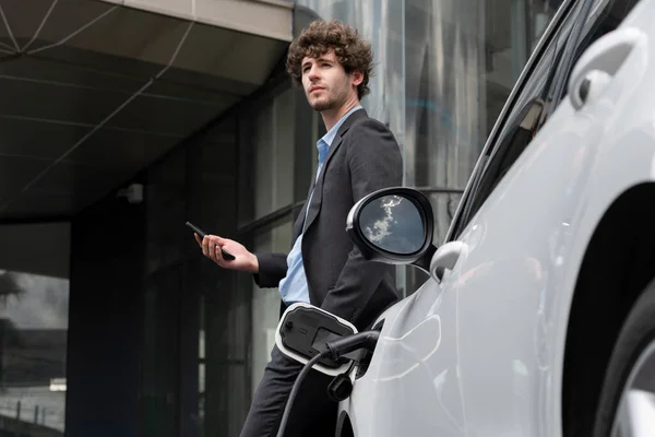 Progressive Businessman Talking Phone Leaning Electric Car Recharging Public Charging — стоковое фото