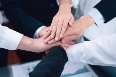 Top view closeup business team of suit-clad businesspeople join hand stack together. Colleague collaborate and work together to promote harmony and teamwork concept in office workplace.
