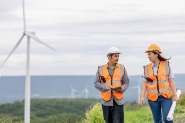 Erkek ve kadın mühendisler kırsal kesimdeki bir tepenin tepesinde ya da dağda rüzgar çiftliğinde çalışıyorlar. Yenilenebilir ve sürdürülebilir enerjinin gelecekteki üretimi için yenilikçi idealler.
