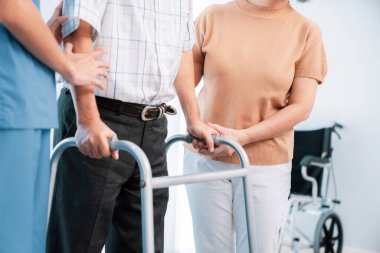 Contented senior man was helped on folding walking by his wife and caregiver. Recuperation for elderly, seniors care, nursing home.