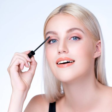 Closeup personable woman with blond hair putting black mascara with brush in hand on long thick eyelash. Perfect fashionable cosmetic clean facial skin with beautiful eye young woman.