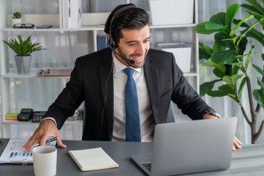 Erkek çağrı merkezi operatörü ya da telesales temsilcisi ofis masasında otururken kulaklık takıyor ve müşteri desteği sağlayan ya da ikna edici satış yapan müşteriyle sohbet ediyor. coşkulu