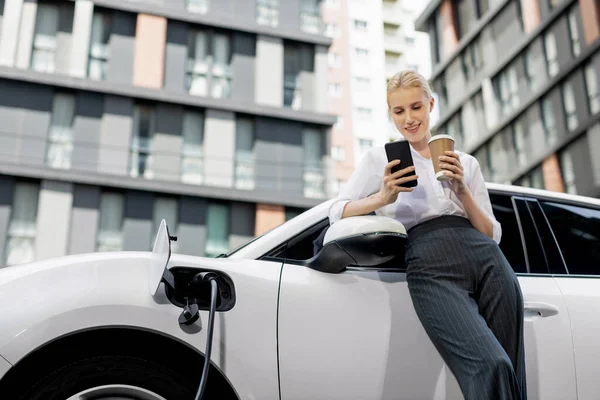 Focus Businessman Using Phone Leaning Electric Vehicle Holding Coffee Blurred — Φωτογραφία Αρχείου