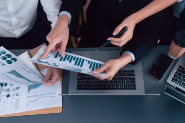 Closeup on BI dashboard on meeting desk with businesspeople analyzing or planning business strategy with hands pointing on financial paper reports as concept of harmony in office workplace.