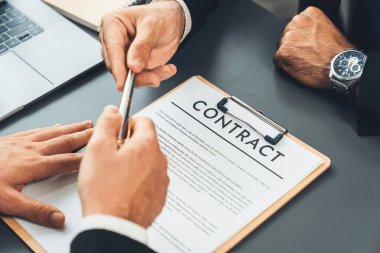 İş anlaşması yapılırken iki işadamı masanın karşısında oturuyor. Şirket avukatı, sözleşmeyi imzalaması için müvekkiline ya da ortağına kalem veriyor ve anlaşmayı imzayla imzalıyor. Coşkulu