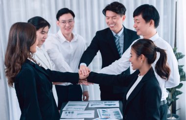 Closeup business team of suit-clad businessmen and women join hand stack together and form circle. Colleague collaborate and work together to promote harmony and teamwork concept in office workplace.