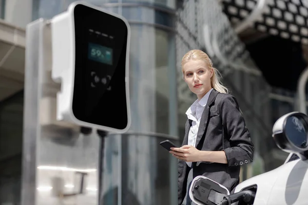 Businesswoman Wearing Black Suit Using Smartphone Leaning Electric Car Recharge — Foto Stock