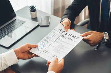 Resmi ofiste takım elbise giyen kendine güvenen bir adam, iş görüşmesi sırasında özgeçmiş kağıtlarını tutuyor. Sorular soran, aday yeterliliği ve iş için uygunluk değerlendirmesi yapan bir muhabir. Coşkulu