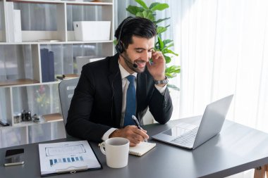 Erkek çağrı merkezi operatörü ya da telesales temsilcisi ofis masasında oturmuş kulaklık takıyor ve müşteri hizmetleri desteği sağlayan ya da satış yapan müşteriyle sohbet ediyor. coşkulu