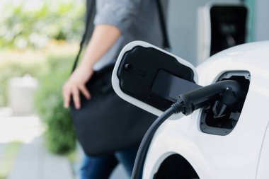 Focus electric car charging at home charging station with blurred progressive man walking in the background. Electric car using renewable clean for eco-friendly concept.
