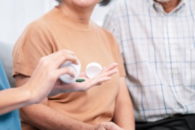 Contented senior woman sit along side with her husband, taking medicines while her caregiver advising her medication. Medication for seniors, nursing house, healthcare at home.