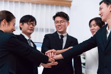 Closeup business team of suit-clad businessmen and women join hand stack together and form circle. Colleague collaborate and work together to promote harmony and teamwork concept in office workplace.