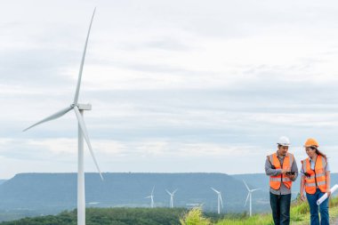 Erkek ve kadın mühendisler kırsal kesimdeki bir tepenin tepesinde ya da dağda rüzgar çiftliğinde çalışıyorlar. Yenilenebilir ve sürdürülebilir enerjinin gelecekteki üretimi için yenilikçi idealler.