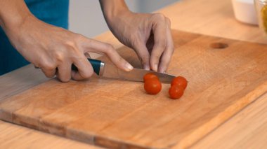 Close up hands holding a knife preparing a contented meal. Sliced tomatoes and other vegetables on the glass dish.
