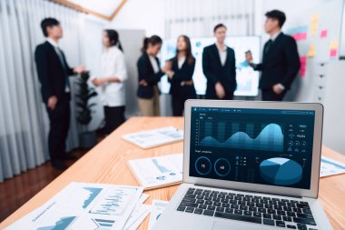 Focus laptop monitor display dashboard report by business intelligence, analyzed financial data for planning market strategy with blur background of standing office worker discussing in harmony office