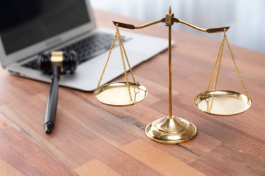 Adalet ve hukuki otoriteyi temsil eden, altın dengeli ölçek ve hukuk bürosunda dizüstü bilgisayarlı tokmak, avukat ve hakimin eşitlik ve adil yargılama kavramını yansıtıyor. denge