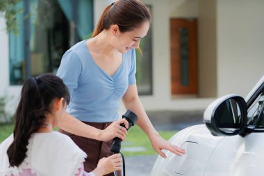 Evde şarj edilen elektrikli bir araçla okuldan yeni dönen anne ve kızın ilerici yaşam tarzı. Elektrikli araç, sürdürülebilir temiz enerjiyle çalışıyor..