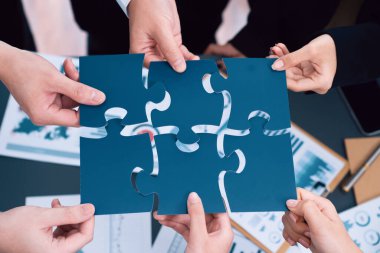 Closeup top view business team of office worker putting jigsaw puzzle together over table filled with financial report paper in workplace with manager to promote harmony concept in meeting room.