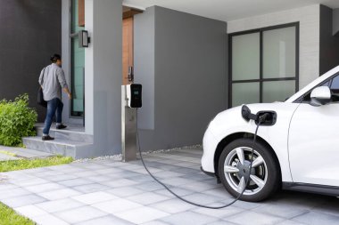 Progressive asian man and electric car with home charging station. Concept of the use of electric vehicles in a progressive lifestyle contributes to a clean and healthy environment.