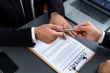 İş anlaşması yapılırken iki işadamı masanın karşısında oturuyor. Şirket avukatı, sözleşmeyi imzalaması için müvekkiline ya da ortağına kalem veriyor ve anlaşmayı imzayla imzalıyor. Coşkulu