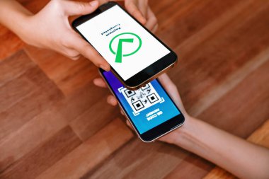 QR kodu parasız ödeme taraması için ekranda gösterilir. Kapalı eller, mobil uygulamadan elektronik işlem yoluyla para aktarmak için akıllı telefonu tutuyor. Hızlı ödeme için barkod teknolojisi. Coşkulu.