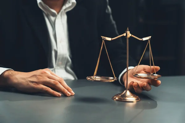 stock image Lawyer in a black suit sits attentively on his office desk with a golden scale balance, symbol of legal justice and integrity, balanced and ethical decision making in the court of law. equility