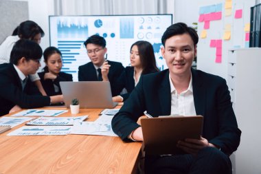 Focus portrait of successful confident male manager or executive in business wear with blurred background of businesspeople, colleagues working with financial report papers in office of harmony.