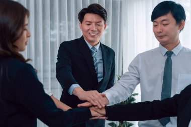Closeup business team of suit-clad businessmen and women join hand stack together and form circle. Colleague collaborate and work together to promote harmony and teamwork concept in office workplace.