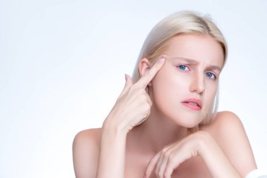 Acne problem troubling personable worried woman with natural beauty skin checking her face squeezing pimple spots in isolated background. Copyspace for blemish skincare treatment problem.