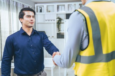 An engineer with a protective vest handshake with an investor in his office. Following a successful meeting, employee and employer form a partnership.